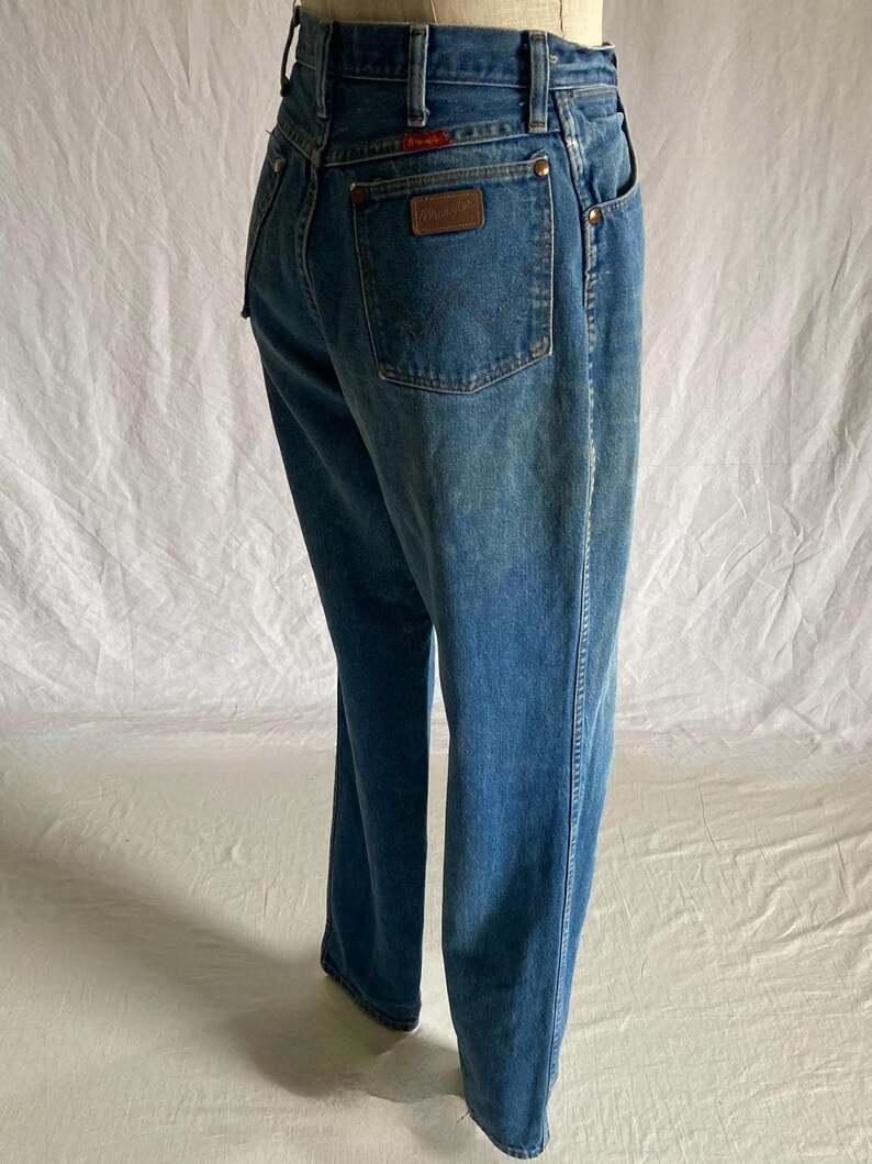 Pu&ograve; includere: Jeans in denim blu dalla vestibilit&agrave; classica. Presentano una toppa in pelle marrone sulla tasca posteriore con il marchio Wrangler e rivetti color rame. I jeans hanno un lavaggio sbiadito e una gamba dritta.