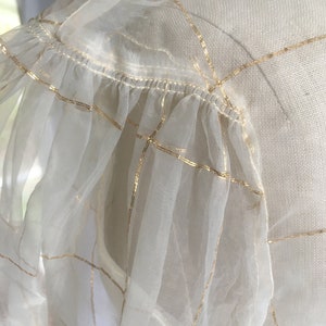 May include: White sheer fabric with gold grid pattern and a ruffled edge.