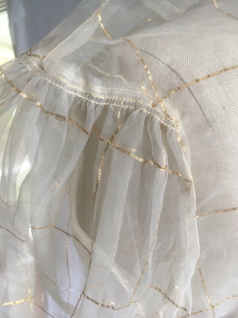 May include: White sheer fabric with gold grid pattern and a ruffled edge.