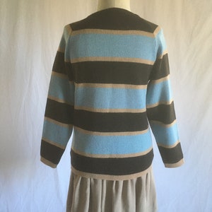 May include: A striped sweater with brown, light brown, and blue horizontal stripes. The sweater has long sleeves and a crew neck. The sweater is being displayed on a mannequin wearing a beige skirt.