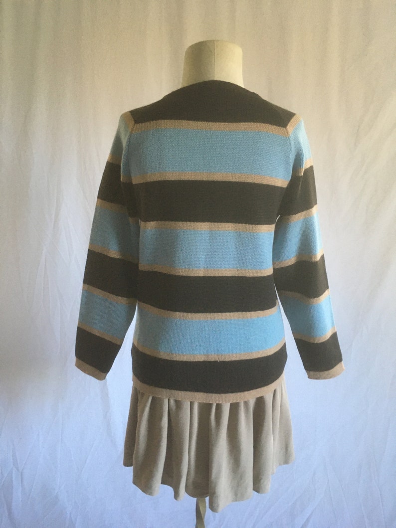 May include: A striped sweater with brown, light brown, and blue horizontal stripes. The sweater has long sleeves and a crew neck. The sweater is being displayed on a mannequin wearing a beige skirt.
