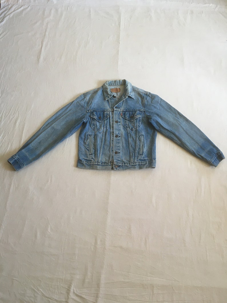 May include: A light blue denim jacket with a button closure and two front pockets.