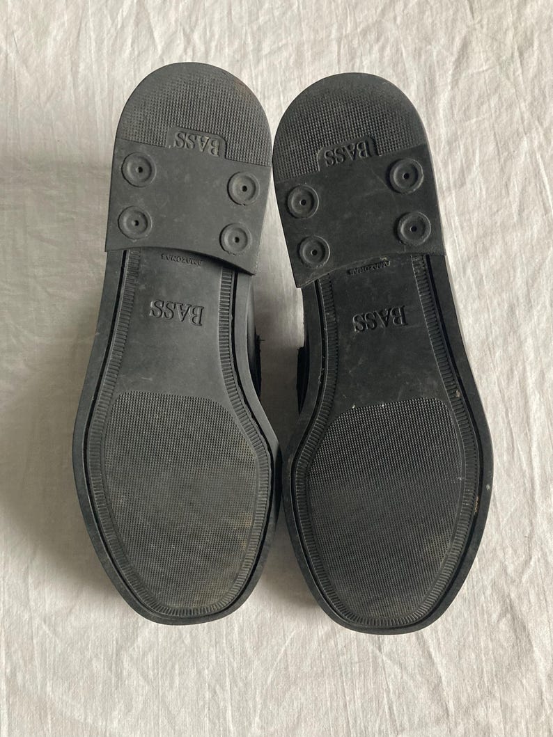 May include: Two black shoe soles are shown, revealing the textured rubber undersides. The soles are branded with "BASS" and have a grip pattern. The shoes appear to be in good condition.
