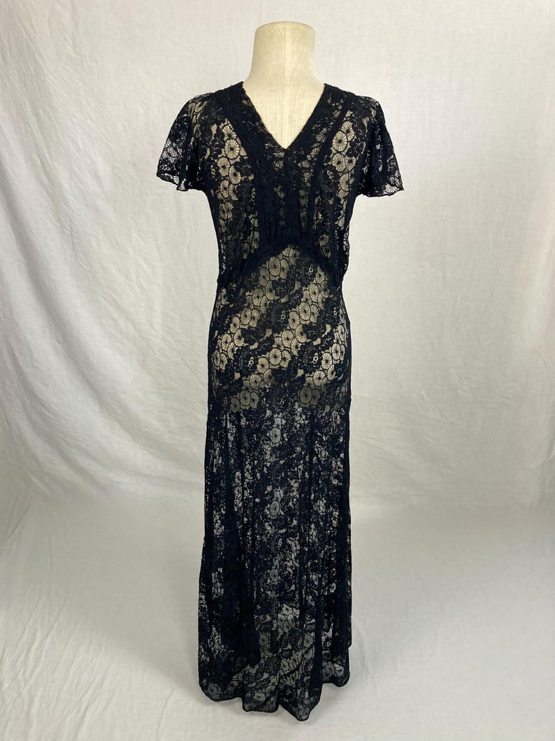 May include: A black lace maxi dress with a V-neckline and short sleeves. The dress is sheer and has a floral pattern.