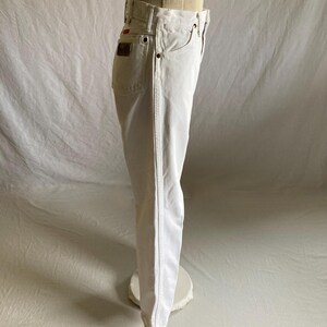 May include: White denim jeans with a classic five-pocket design. The jeans have a straight leg cut and a red logo patch on the back pocket. The jeans are displayed on a mannequin.