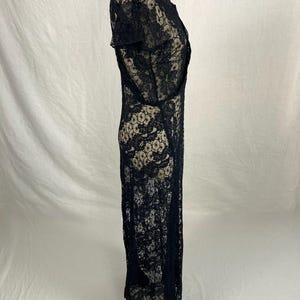 May include: A black lace maxi dress with a scoop neck and short sleeves. The dress is made of a delicate, sheer fabric and has a flowing silhouette.
