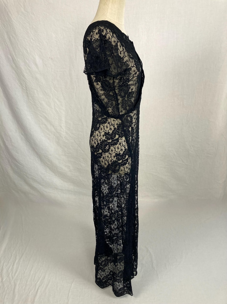 May include: A black lace maxi dress with a scoop neck and short sleeves. The dress is made of a delicate, sheer fabric and has a flowing silhouette.