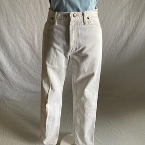 May include: White denim jeans with a button and zip fastening. The jeans have a classic five-pocket design and a straight leg fit. The jeans are displayed on a mannequin with a light blue t-shirt.