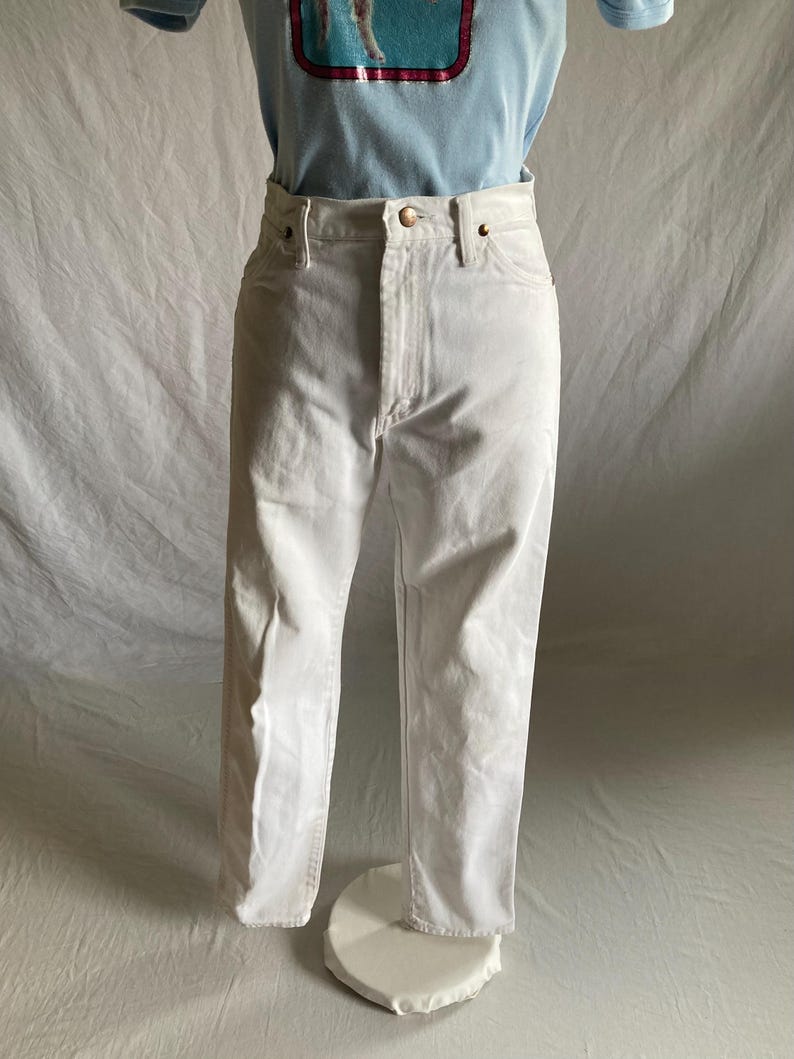 May include: White denim jeans with a button and zip fastening. The jeans have a classic five-pocket design and a straight leg fit. The jeans are displayed on a mannequin with a light blue t-shirt.