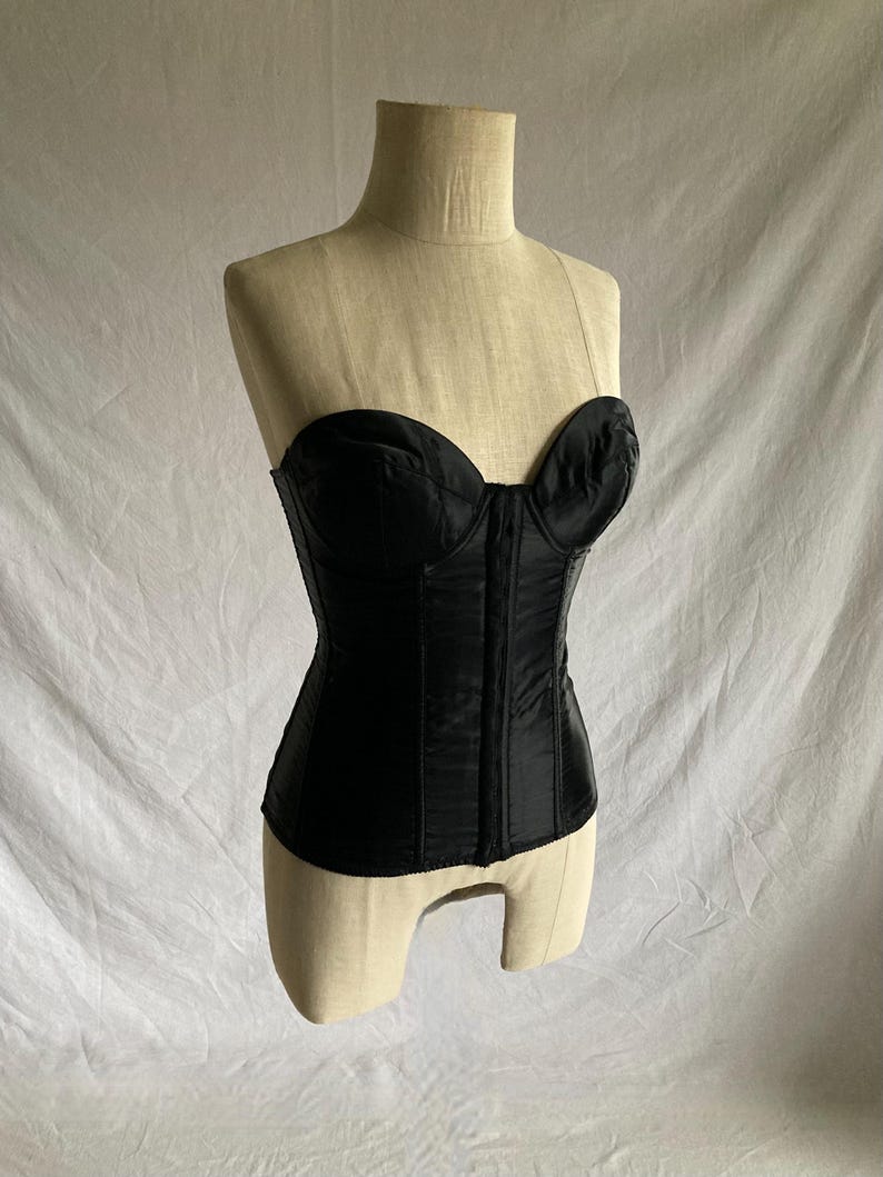 May include: A black strapless corset with boning and a hook and eye closure in the back.