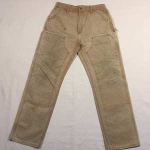 Puede incluir: Un par de pantalones de trabajo de color beige con varios bolsillos y signos visibles de desgaste.