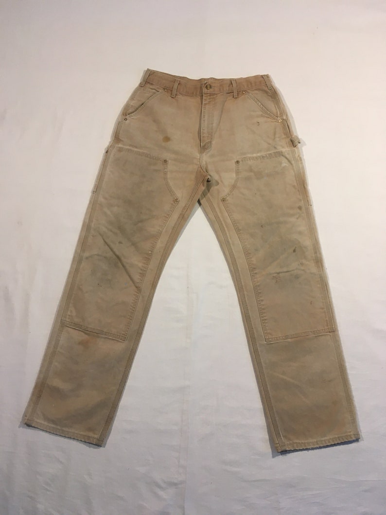 Puede incluir: Un par de pantalones de trabajo de color beige con varios bolsillos y signos visibles de desgaste.