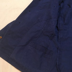 May include: A dark blue work jacket with a single pocket on the left side. The jacket has several small holes in the fabric.