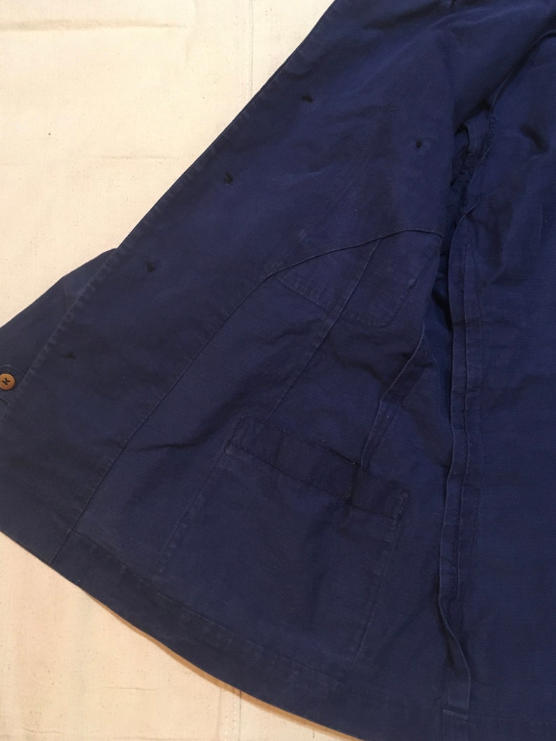 May include: A dark blue work jacket with a single pocket on the left side. The jacket has several small holes in the fabric.