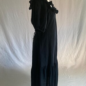 May include: A black maxi dress with a ruffled neckline and short, puffed sleeves. The dress features a tiered skirt and a tie-back detail. The fabric appears to be a lightweight material, suitable for warmer weather. The dress is displayed on a mannequin.