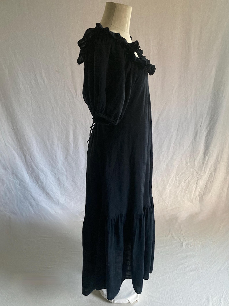 May include: A black maxi dress with a ruffled neckline and short, puffed sleeves. The dress features a tiered skirt and a tie-back detail. The fabric appears to be a lightweight material, suitable for warmer weather. The dress is displayed on a mannequin.