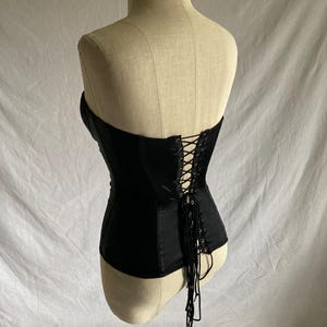 May include: A black satin corset with a lace-up back and a long lace tie. The corset is on a white mannequin.