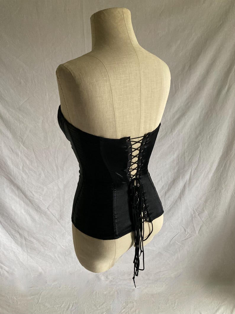May include: A black satin corset with a lace-up back and a long lace tie. The corset is on a white mannequin.