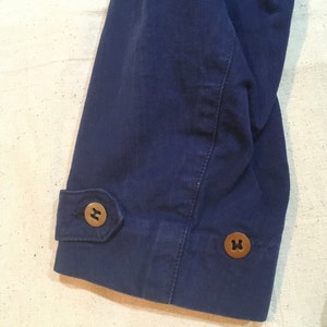 May include: Close-up of the navy blue sleeve of a jacket with two brown buttons. The buttons have a cross-shaped design.
