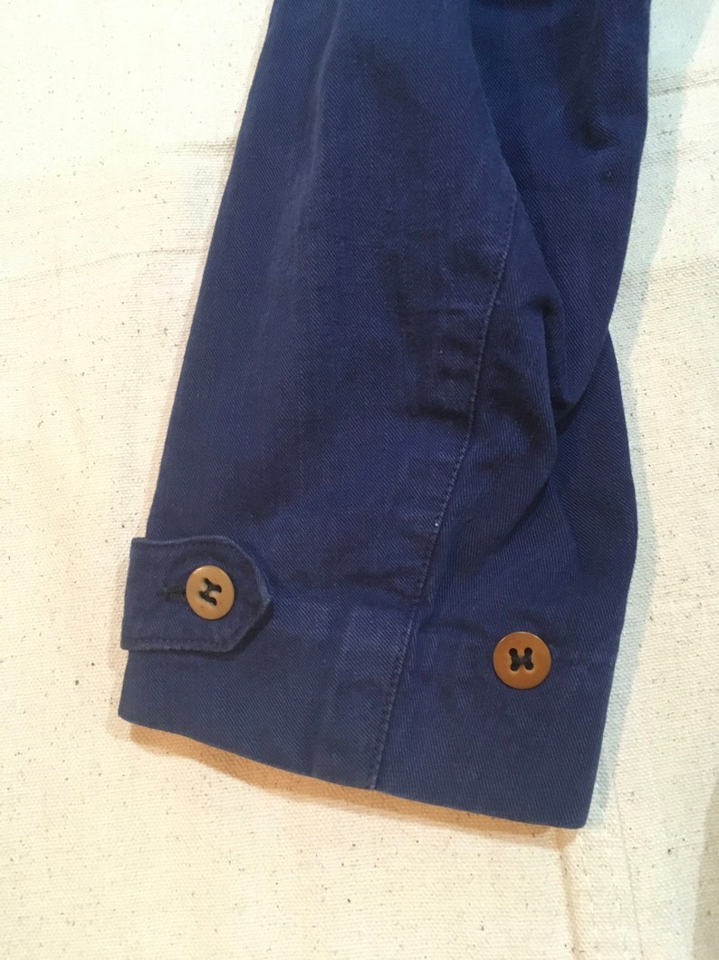 May include: Close-up of the navy blue sleeve of a jacket with two brown buttons. The buttons have a cross-shaped design.