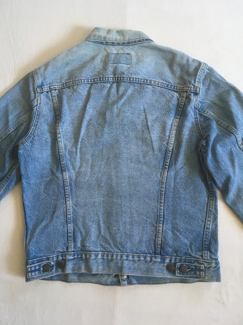 May include: A light blue denim jacket with a button closure and two pockets on the bottom.