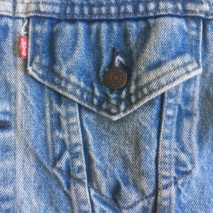 May include: Close-up of a blue denim jacket with a pocket and a metal button. The pocket has a small Levi's label.