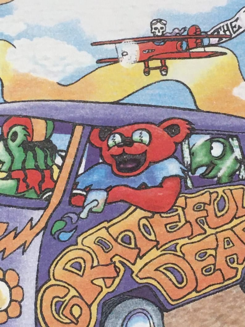 May include: A purple and orange psychedelic van with the words "Grateful Dead" on the side. A red airplane with a skull and crossbones flies above the van. The van has a green creature in the driver's seat and a red bear with sunglasses in the passenger seat.
