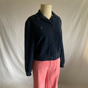 以下が含まれることがあります： ボタン留めのネイビーブルーのコーデュロイジャケットと、お揃いのピンクのコーデュロイパンツ。 ジャケットには襟と2つの小さなポケットが付いています。 パンツはハイウエストで、フレアの脚になっています。