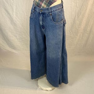 K&ouml;nnte beinhalten: Hellblaue Jeans-Culottes mit rohem Saum. Die Jeans haben ein klassisches F&uuml;nf-Taschen-Design und einen Knopf- und Rei&szlig;verschluss. Die Culottes werden auf einem wei&szlig;en Sockel pr&auml;sentiert, der ihre weitbeinige Silhouette zeigt.