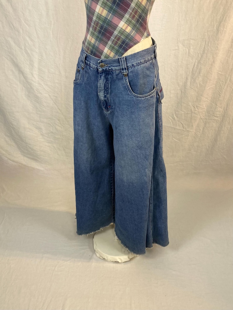 K&ouml;nnte beinhalten: Hellblaue Jeans-Culottes mit rohem Saum. Die Jeans haben ein klassisches F&uuml;nf-Taschen-Design und einen Knopf- und Rei&szlig;verschluss. Die Culottes werden auf einem wei&szlig;en Sockel pr&auml;sentiert, der ihre weitbeinige Silhouette zeigt.