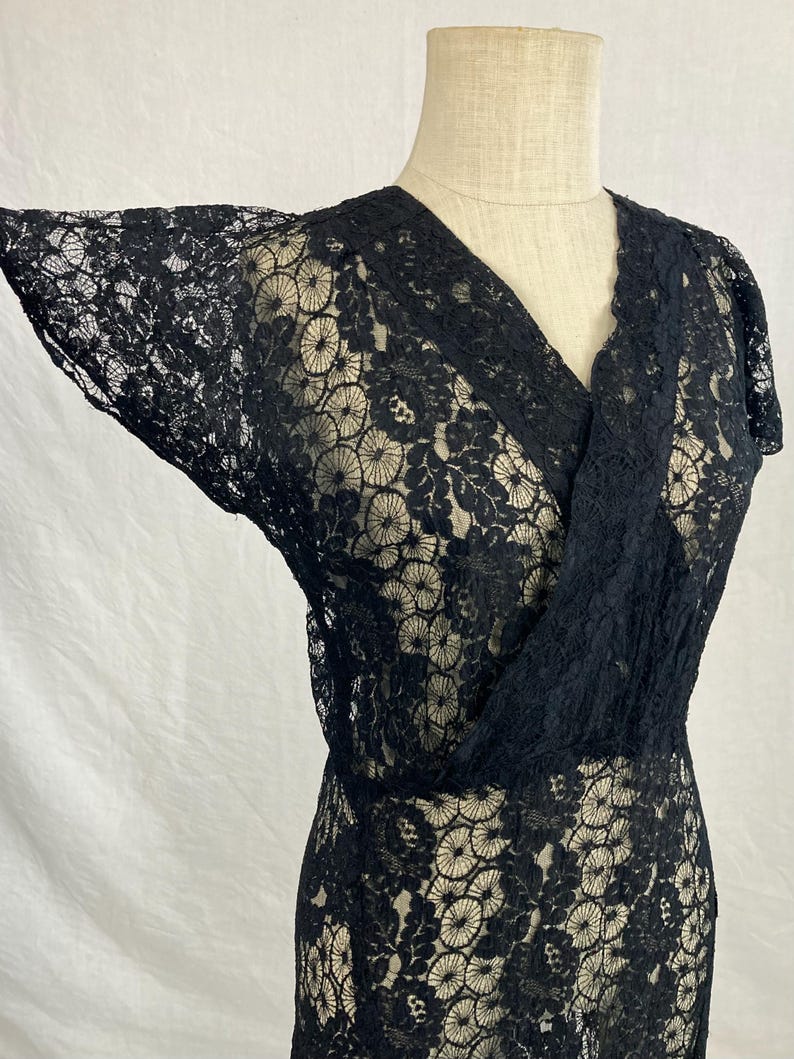 May include: A black lace dress with a V-neckline and short sleeves. The dress has a floral pattern and is made of a delicate fabric.