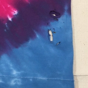 May include: A blue, purple, and pink tie-dye shirt with a small hole near the bottom right corner.