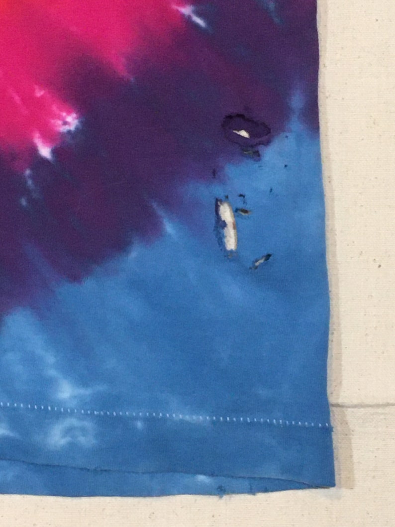 May include: A blue, purple, and pink tie-dye shirt with a small hole near the bottom right corner.
