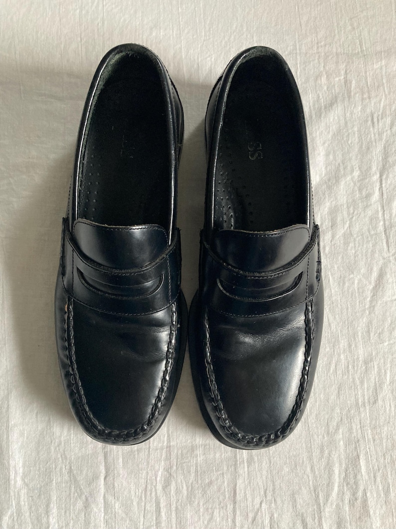 May include: A pair of black leather penny loafers. These shoes feature a classic design with a rounded toe, a strap across the vamp, and a stitched sole. The leather has a glossy finish.