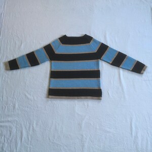 May include: A striped sweater with black, light blue, and beige stripes. The sweater has a round neckline and long sleeves.