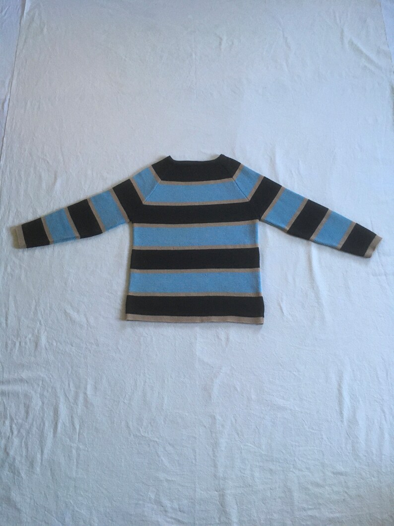 May include: A striped sweater with black, light blue, and beige stripes. The sweater has a round neckline and long sleeves.