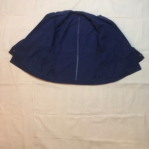 May include: A navy blue jacket with a zipper closure and button accents. The jacket is laid flat and open, showing the inside lining.