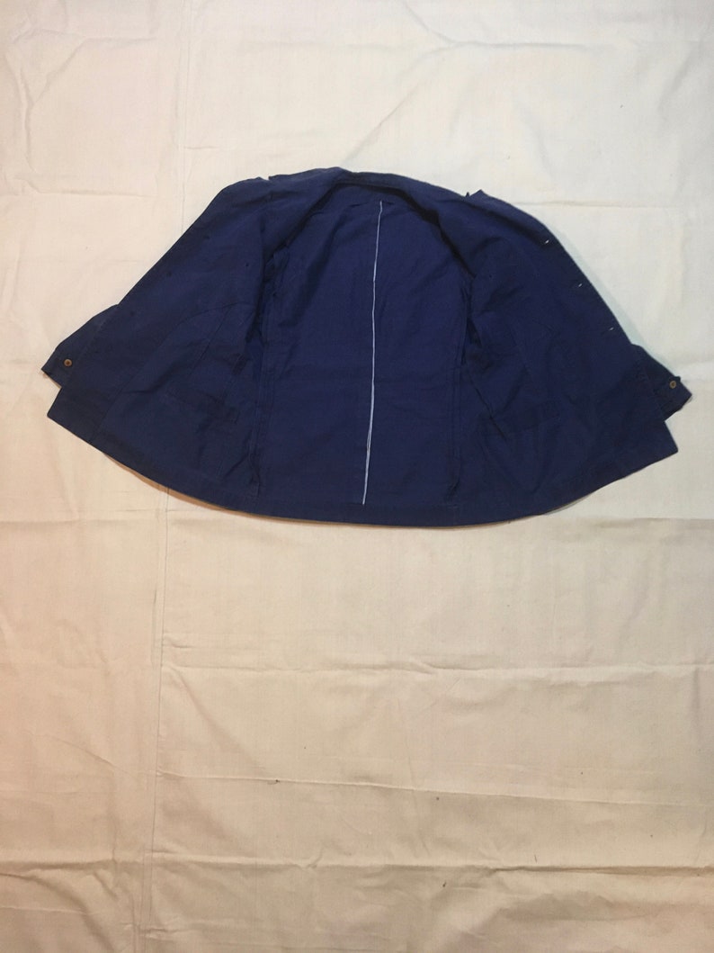 May include: A navy blue jacket with a zipper closure and button accents. The jacket is laid flat and open, showing the inside lining.