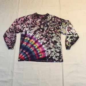 May include: A long-sleeved shirt with a tie-dye pattern in shades of purple, pink, blue, yellow, and white. The shirt has a circular design with a burst of color in the center.
