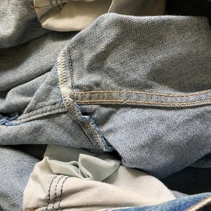 Pu&ograve; includere: Primo piano di jeans in denim blu chiaro, che mostra le tasche interne e i dettagli delle cuciture. Le tasche sono di una tonalit&agrave; di blu pi&ugrave; chiara e le cuciture sono rinforzate con filo a contrasto. Rivetti e bottoni metallici visibili.