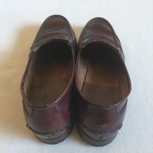 May include: A pair of burgundy leather loafers with a decorative stitch detail around the edges.