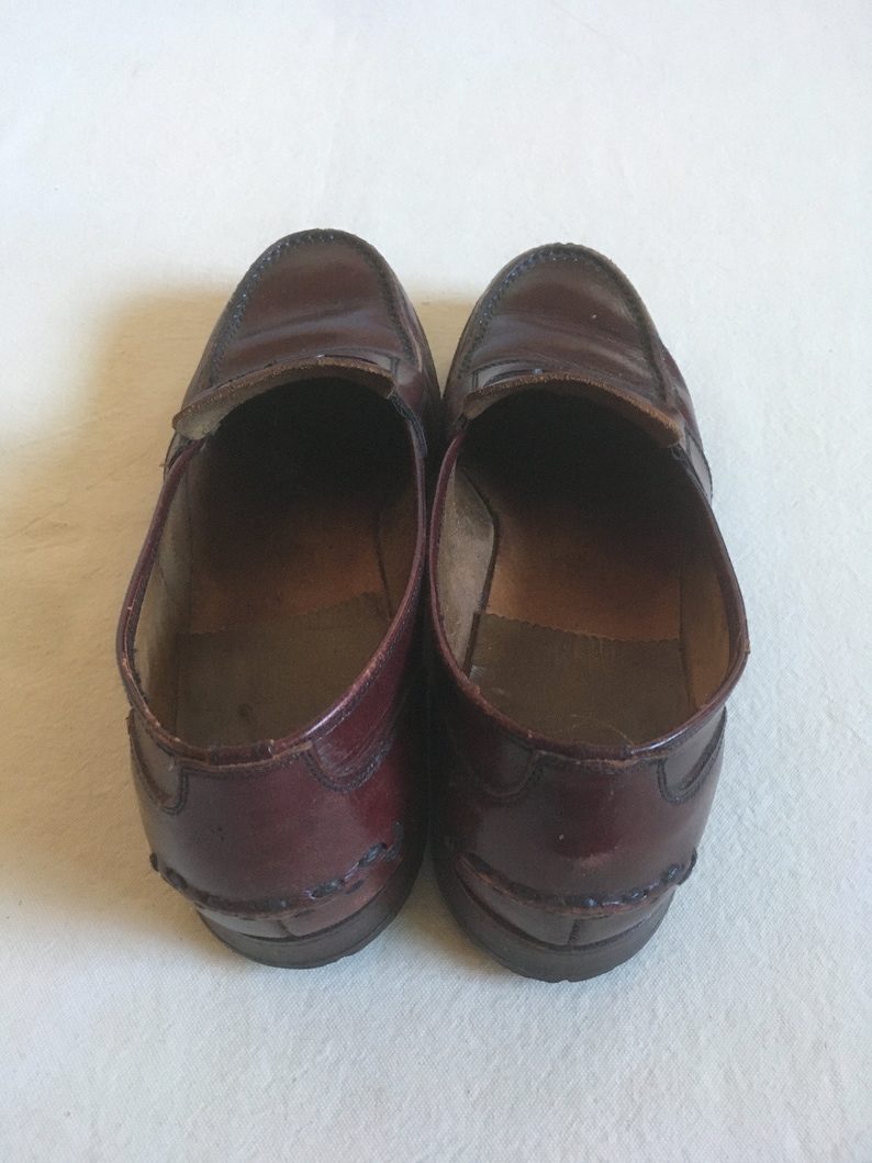 May include: A pair of burgundy leather loafers with a decorative stitch detail around the edges.