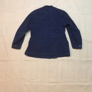 May include: A dark blue work jacket with long sleeves and button closures. The jacket has a simple design and is made of a durable fabric.