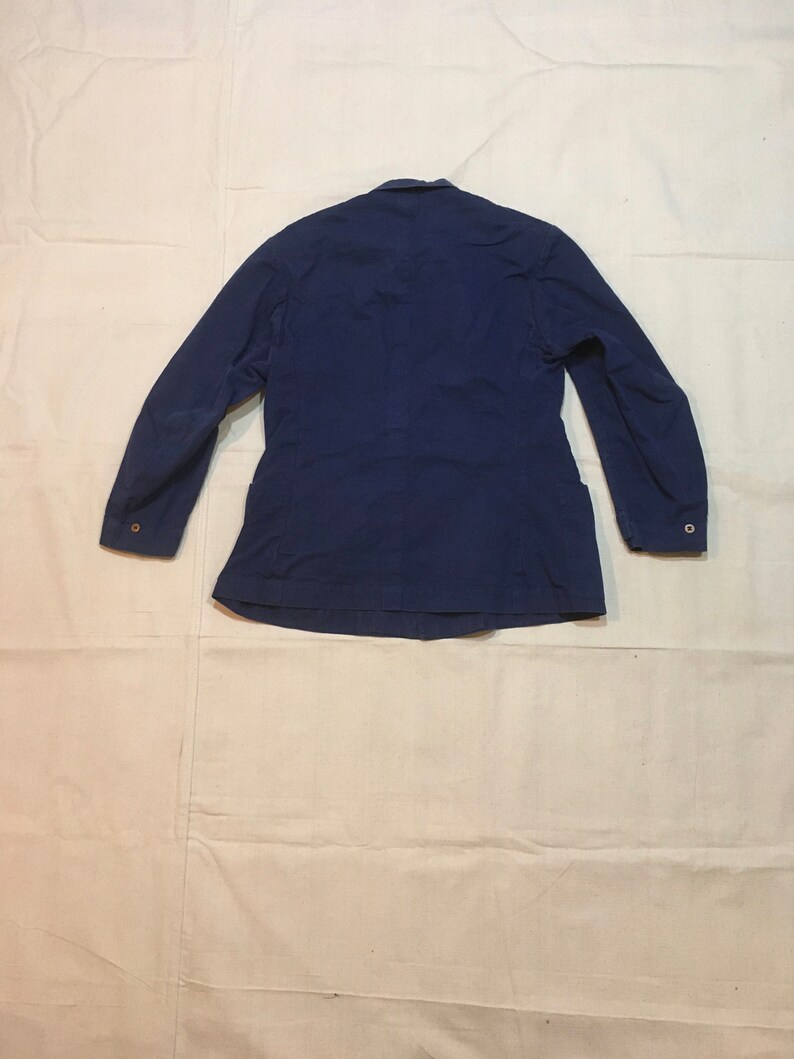 May include: A dark blue work jacket with long sleeves and button closures. The jacket has a simple design and is made of a durable fabric.