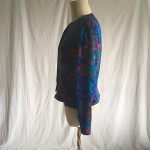 Op de afbeelding: Een teal, paars en roze bloemenprintjasje met een zwarte stropdas aan de hals.