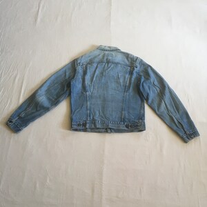 May include: A light blue denim jacket with a button closure and two front pockets.