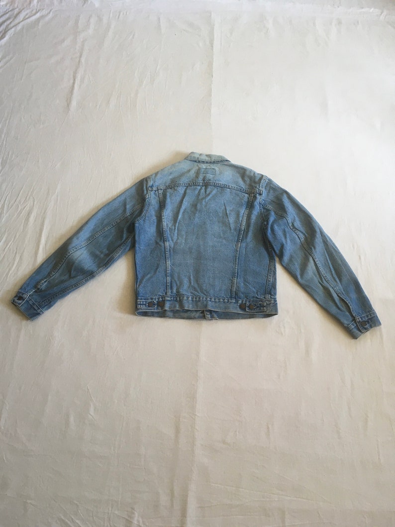 May include: A light blue denim jacket with a button closure and two front pockets.
