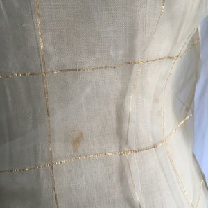 May include: A sheer white fabric with gold thread woven into a grid pattern. The fabric has a few small brown stains.