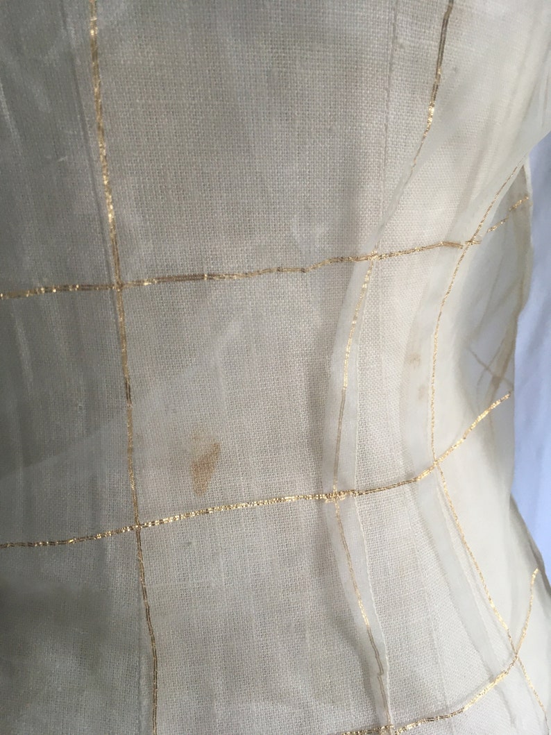 May include: A sheer white fabric with gold thread woven into a grid pattern. The fabric has a few small brown stains.