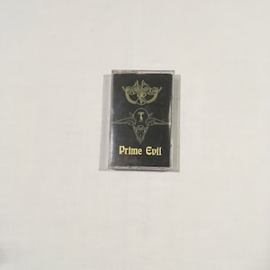 May include: A black cassette tape with a gold design of a winged creature and the text "Prime Evil".